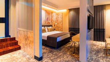 A modern hotel room with a bed, a desk, and a chair. There is a staircase leading to an upper level.