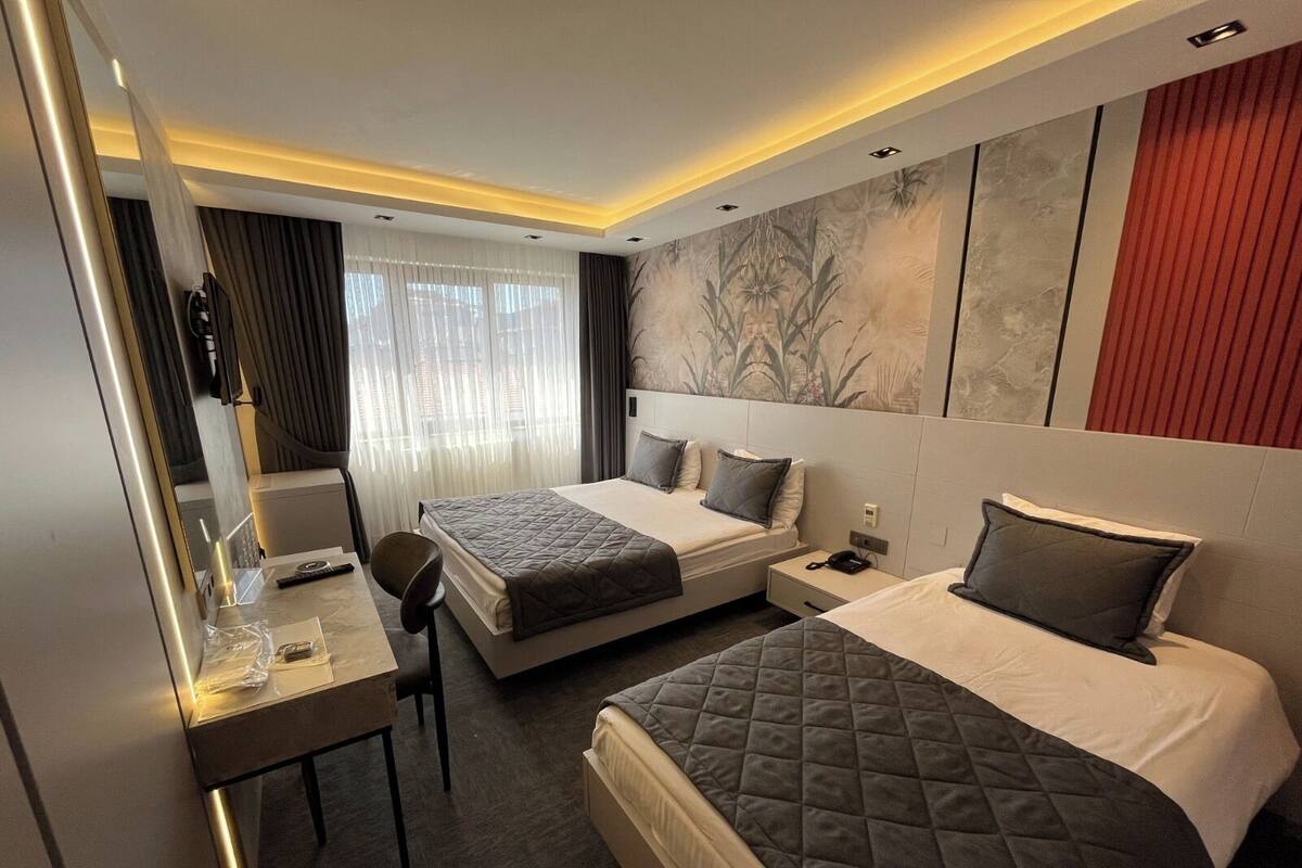 A hotel room with two beds, a desk, a chair, a mirror, and a large window with curtains.