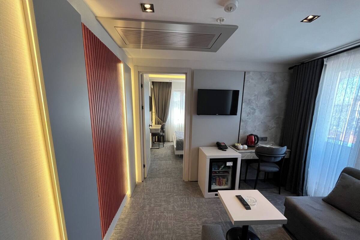 A hotel room with a sofa, a small table, a TV, a kitchenette, and a bathroom visible in the background.