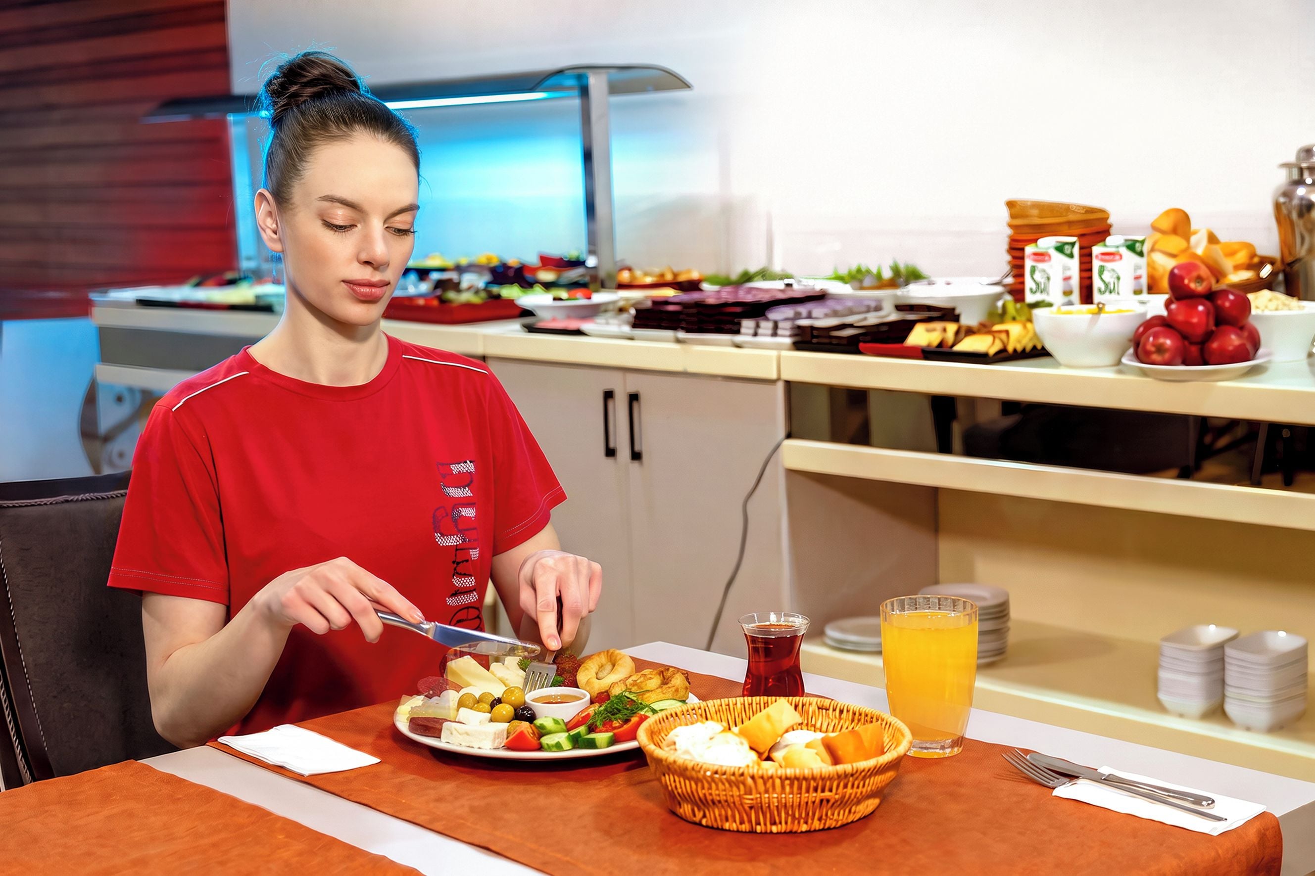 A person seated at a table with a meal, including a plate of food, a glass of juice, and a basket.