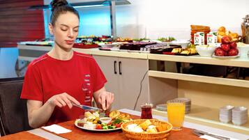A person seated at a table with a meal, including a plate of food, a glass of juice, and a basket.