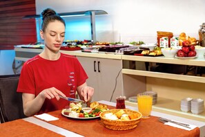 Eine Person sitzt an einem Tisch und isst, mit einem Teller Essen, einem Glas Saft und einem Korb.