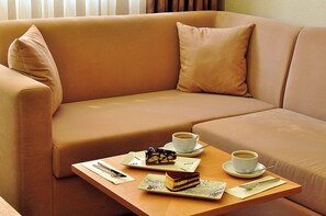 A beige sofa with a tray table in front, holding a cake, two cups of coffee, and a teapot. - Starton Hotel & SPA (Ankara)