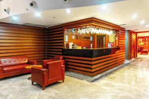 Zona de recepción con un mostrador de madera, un sofá de cuero rojo y una mesita.