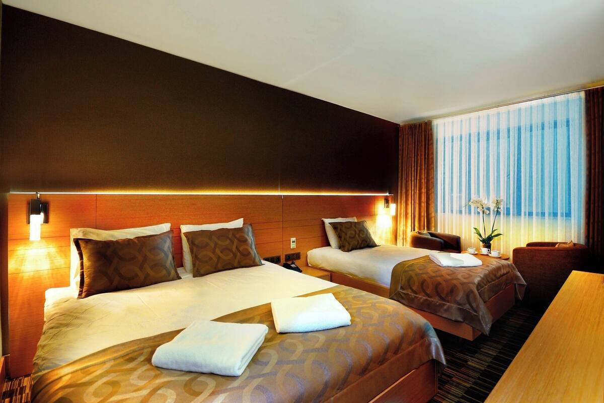 A hotel room with two beds, a desk, a chair, and a large window with curtains.