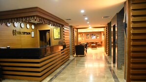 Un espace d’accueil avec un comptoir de réception en bois, plusieurs horloges et un bar visible au fond.