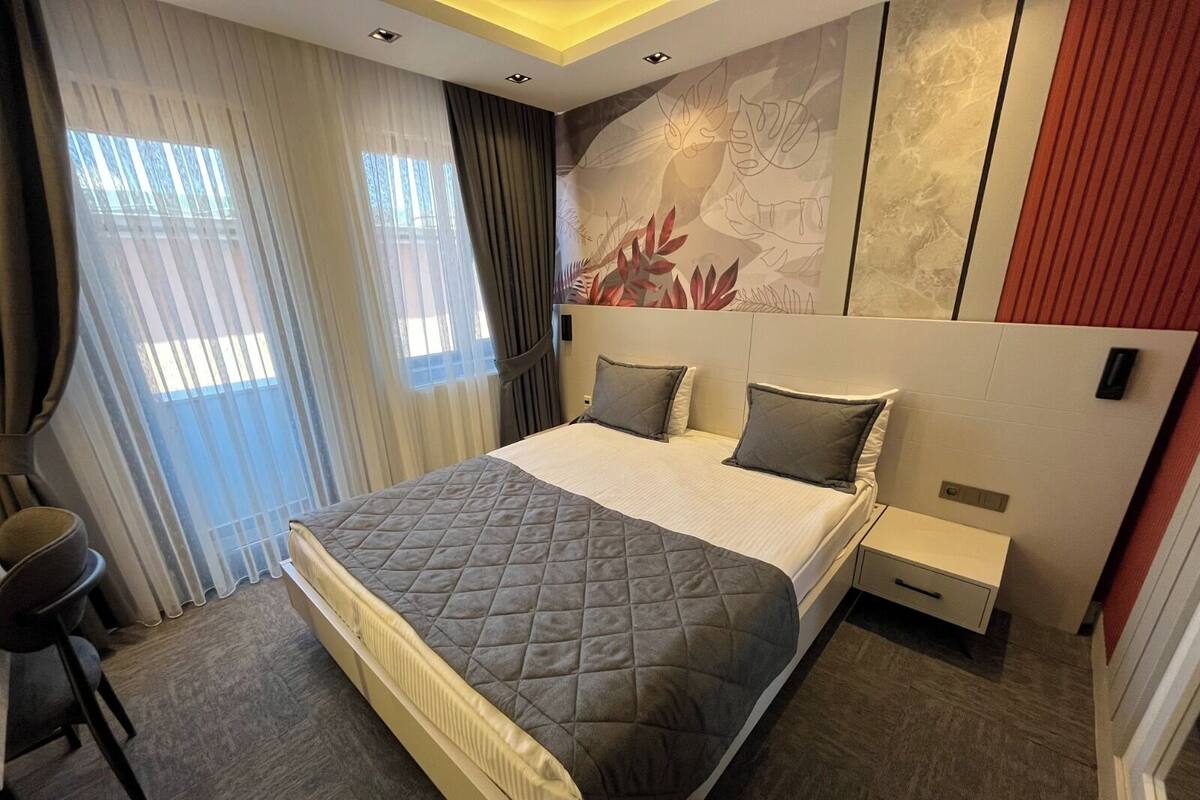 A modern hotel room with a large bed, a nightstand, a chair, and a wall mural.