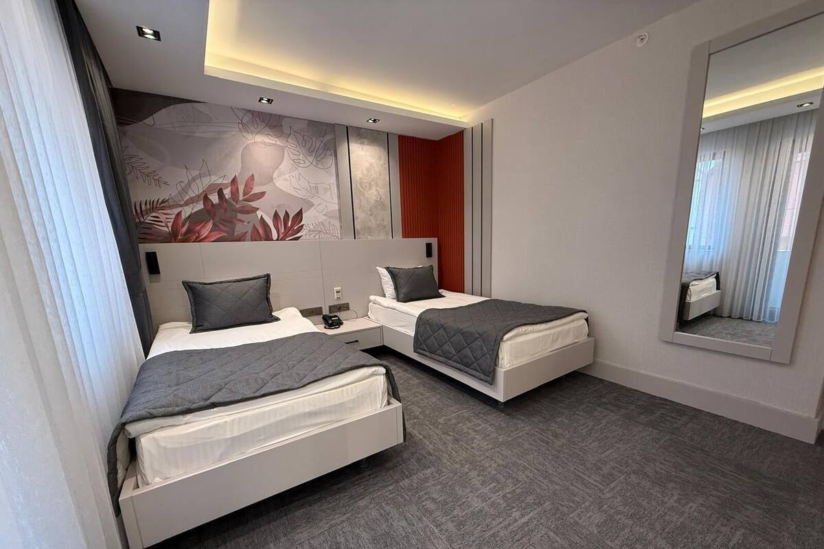 A modern hotel room with two beds, a large mirror, and a decorative wall mural.