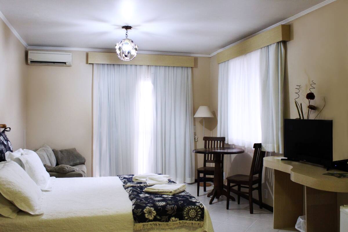 Ein Hotelzimmer mit einem Bett, einem Schreibtisch mit Fernseher, einem Sessel und einer Lampe.