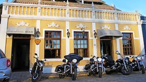 A yellow building with a bar sign, multiple motorcycles parked in front, and a clear blue sky. - Hotel Solar da Beira (São Francisco do Sul)