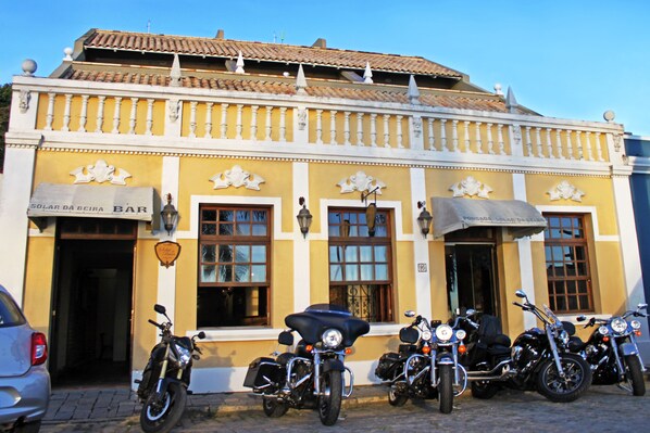 Ein gelbes Gebäude mit einer Bar-Beschilderung, vor der mehrere Motorräder geparkt sind, und ein klarer, blauer Himmel.