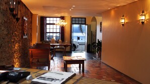 A hotel lobby with a stone wall, wooden furniture, a tiled floor, and a view of the beach through a large window. - Hotel Solar da Beira (São Francisco do Sul)
