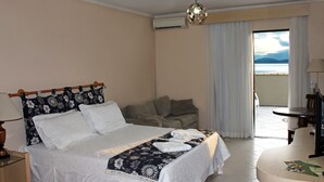 A hotel room with a bed, a sofa, a dining table, and a view of the sea. - Hotel Solar da Beira (São Francisco do Sul)