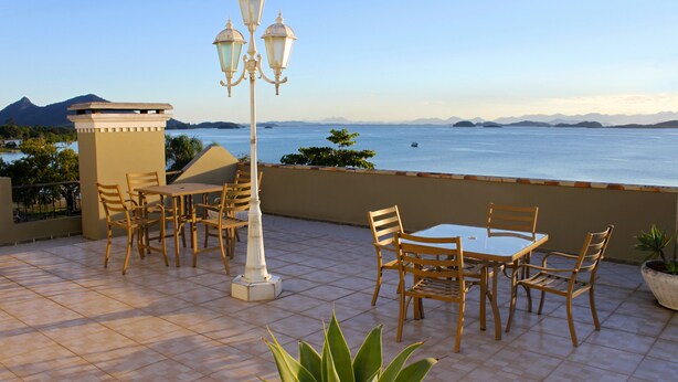 A terrace with a table and chairs, a lamp post, and a view of the sea. - Hotel Solar da Beira (São Francisco do Sul)