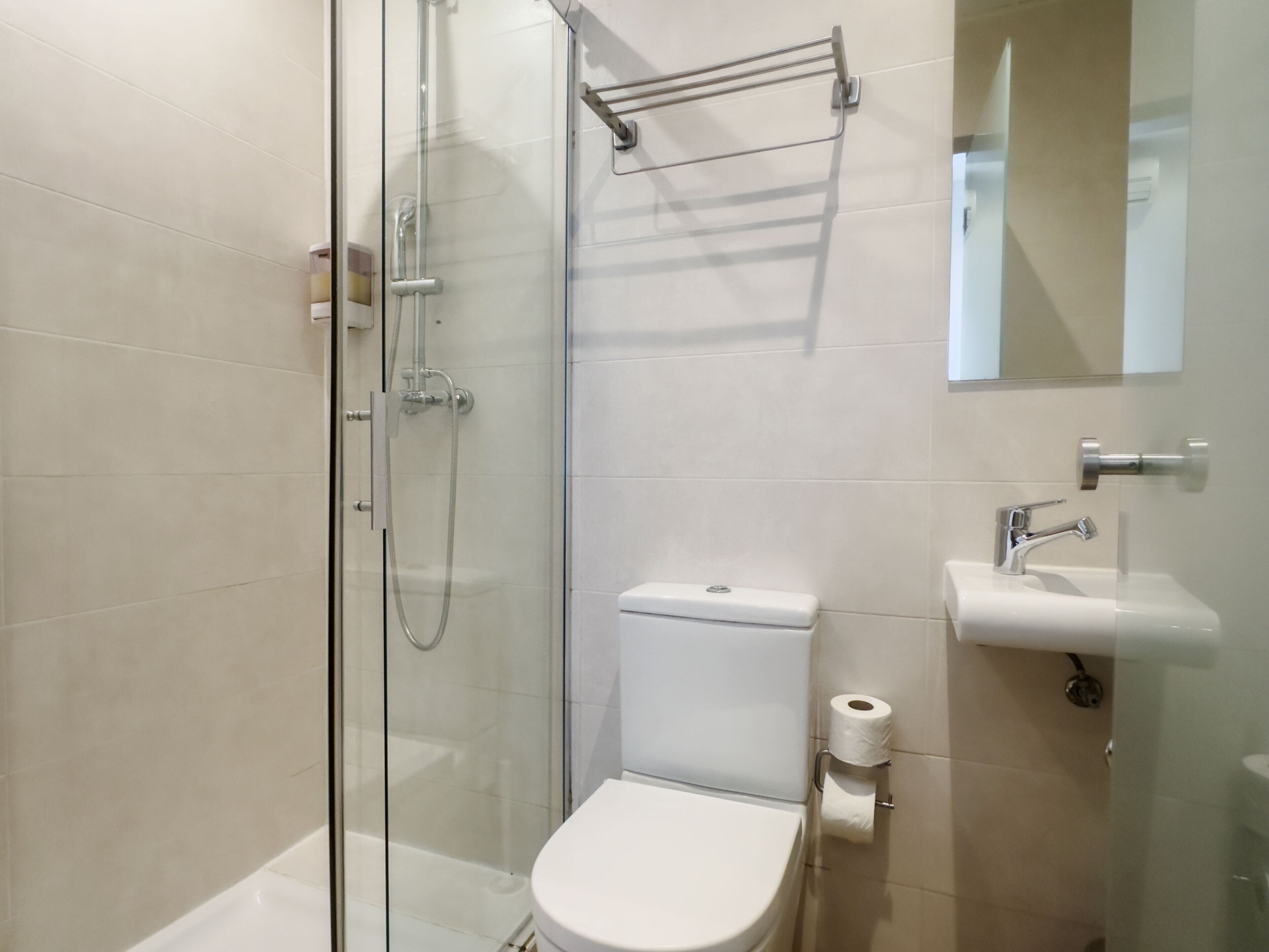Une salle de bain moderne avec une douche à parois de verre, des toilettes blanches et un lavabo surmonté d’un miroir.