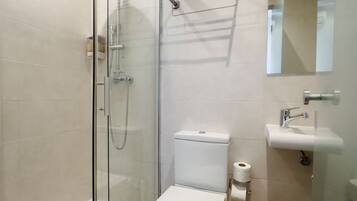Une salle de bain moderne avec une douche à parois de verre, des toilettes blanches et un lavabo surmonté d’un miroir.
