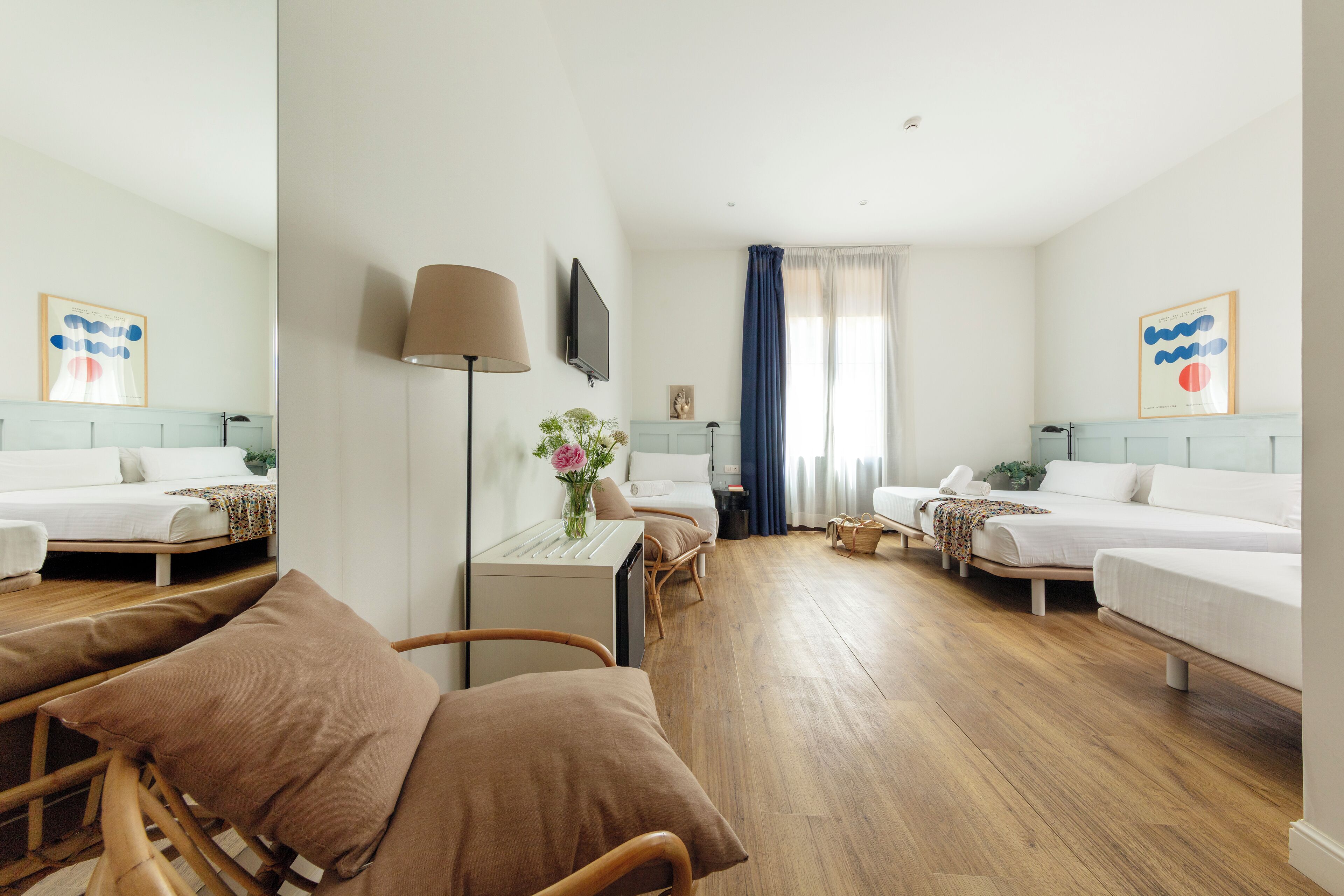 Habitación de hotel con dos camas individuales, un escritorio con lámpara, un televisor y una ventana con cortinas.