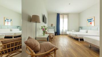 Habitación de hotel con dos camas individuales, una zona de estar con una silla y una mesa, un televisor montado en la pared y un ventanal con cortinas.