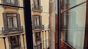 Une vue à travers une porte vitrée d’un immeuble doté de nombreux balcons, chacun étant pourvu de garde-corps en métal et de fenêtres avec des volets.