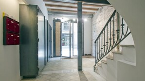 Un pasillo con piso de baldosas, una escalera con barandal de metal y una puerta que da a otra habitación.
