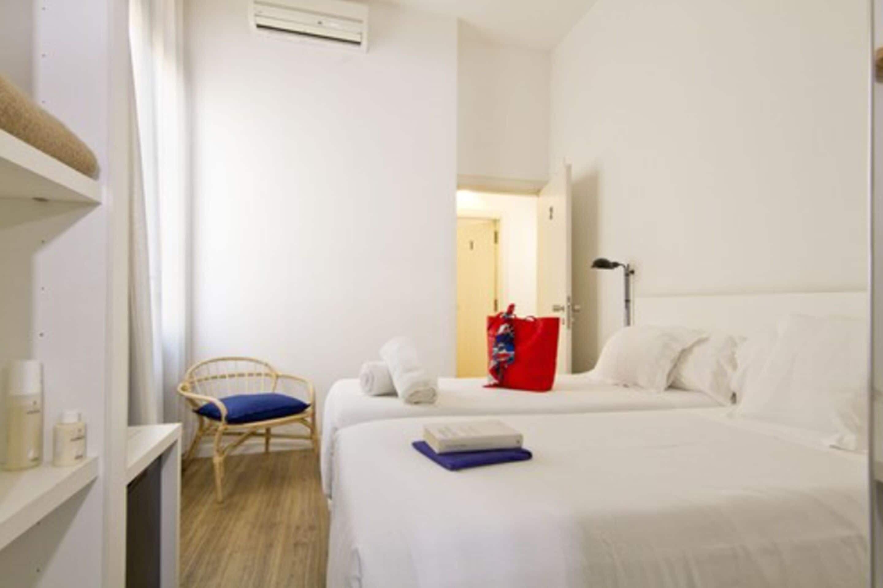 Habitación de hotel con dos camas, una silla, un bolso rojo y una lámpara.