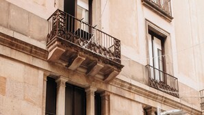 Un edificio con una entrada amplia, un balcón con barandillas de metal ornamentadas y una puerta visible marcada con una 'P' para estacionamiento.