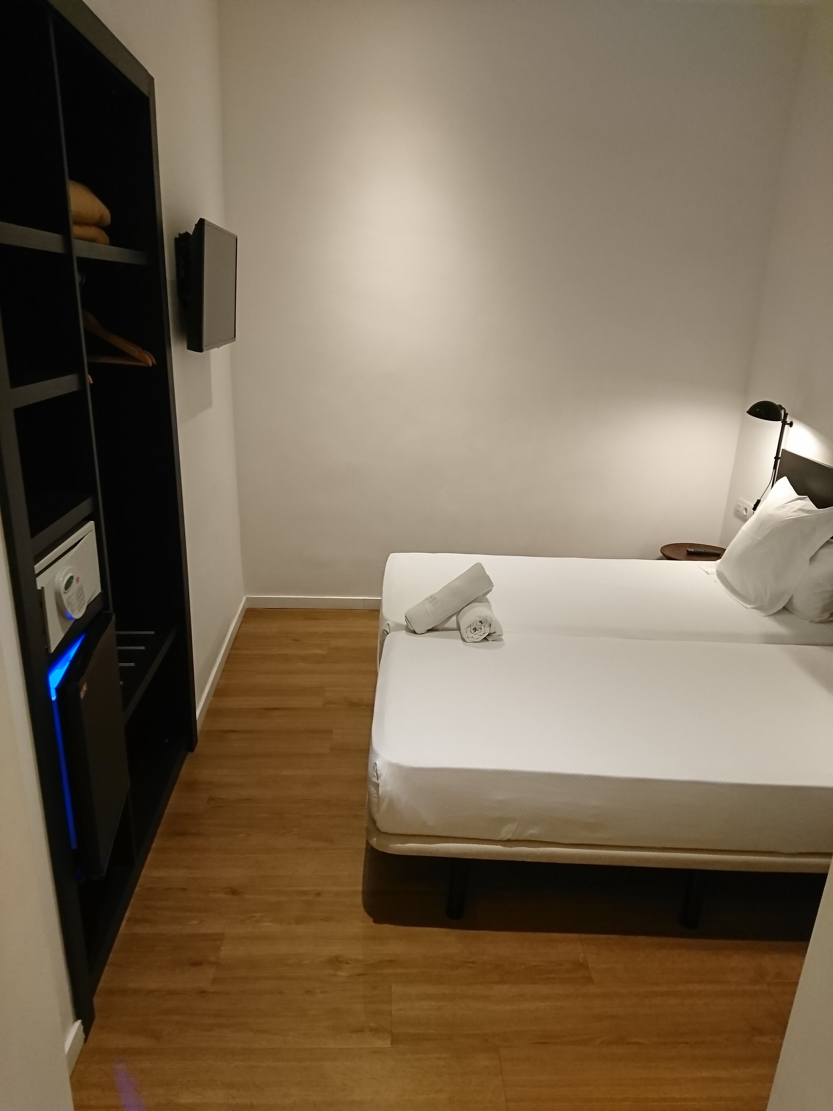 Een compacte, verzorgde slaapkamer met een bed, nachtkastje, lamp en kledingkast.