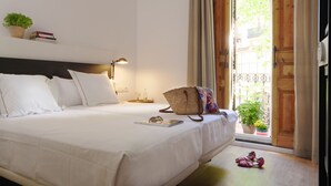 A neatly made bed with white linens, a bedside lamp, a small table with a glass, and a potted plant on the windowsill. - Som Nit Triomf (Barcelona)