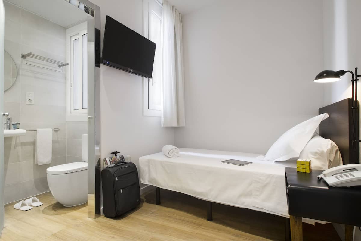 Habitación de hotel con cama, mesita de noche, televisión y un pequeño escritorio con lámpara.