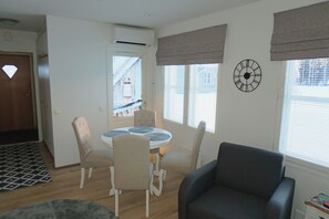 Ein Wohnzimmer mit rundem Tisch, vier Stühlen, einem Sofa, einer Uhr und einem Fenster mit Jalousien.