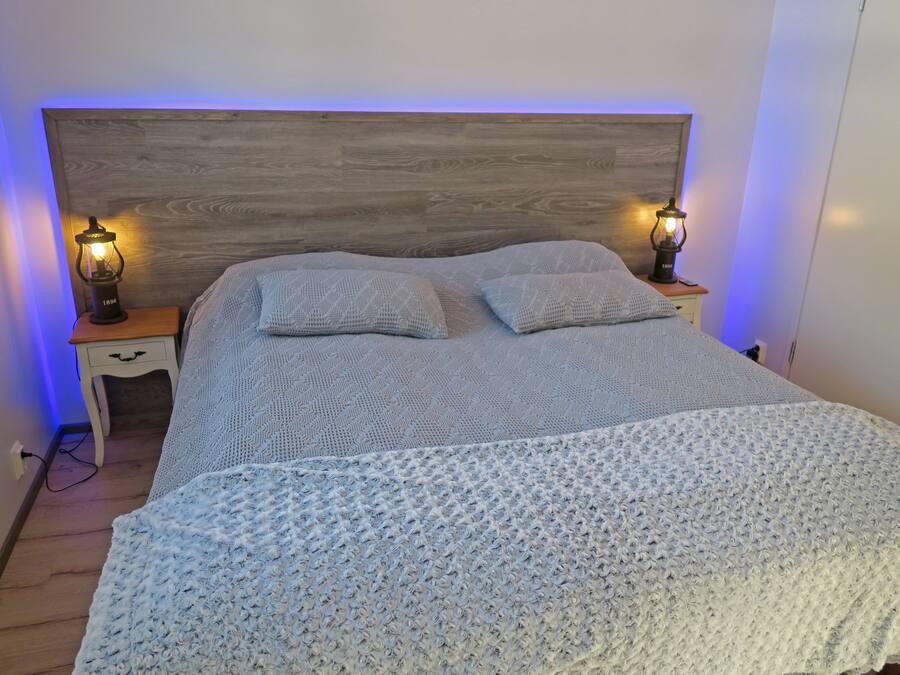 A bedroom with a wooden headboard, two bedside tables with lamps, a knitted blanket, and two pillows.