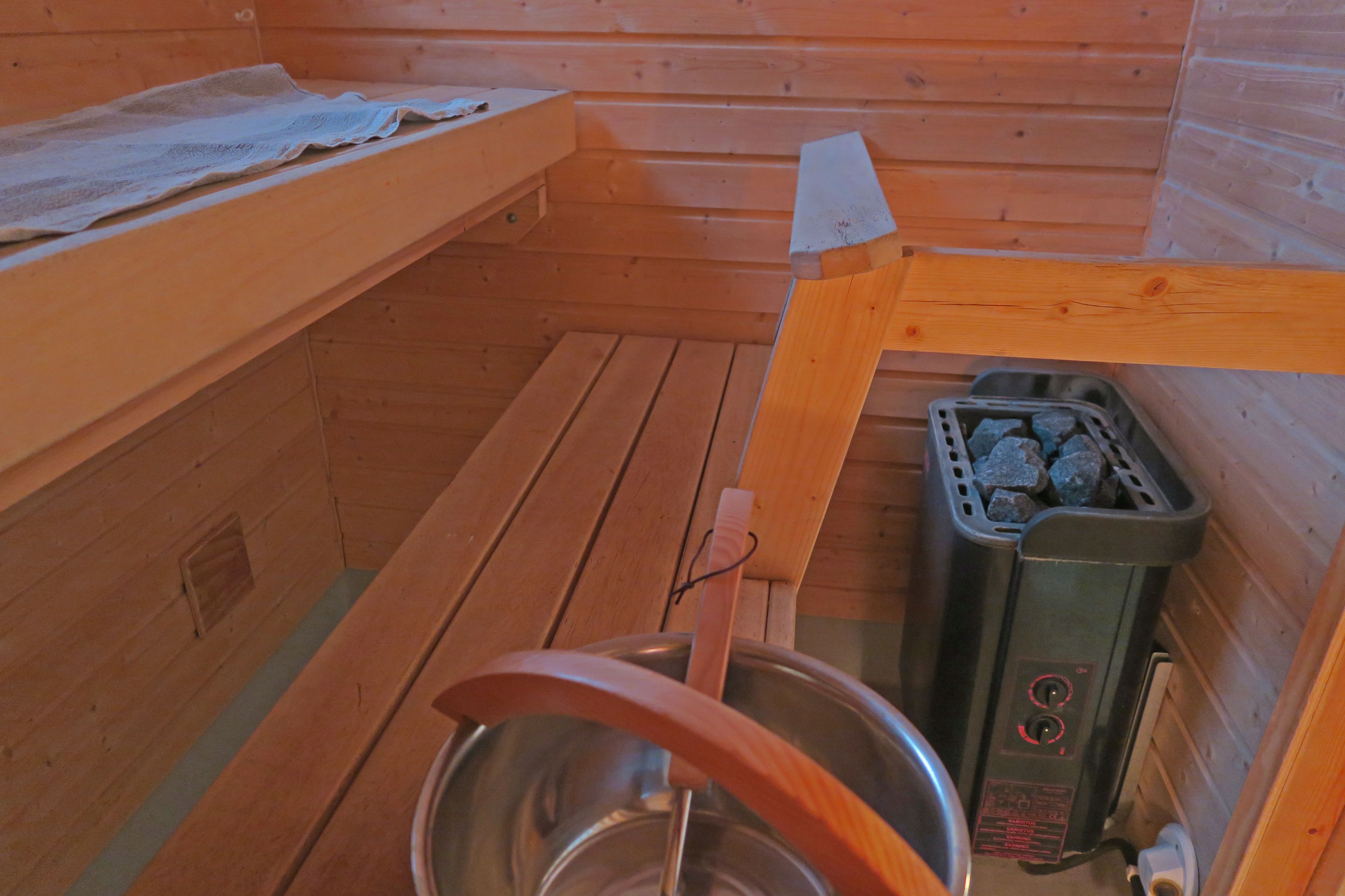 A sauna room with wooden benches, a metal basin, and a sauna heater.