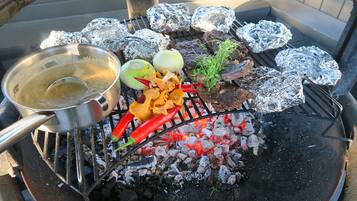 Una parrilla con alimentos envueltos en papel de aluminio, una olla y verduras.