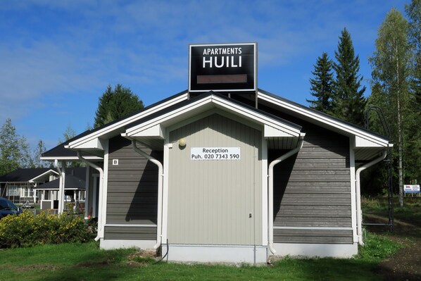 A small building with a sign reading "Apartments HUILI" and a reception desk with a phone number. - Apartments Huili (Kuopio)