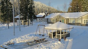 A snow-covered outdoor area with a wooden swing set, picnic tables, and a gazebo. - Apartments Huili (Kuopio)