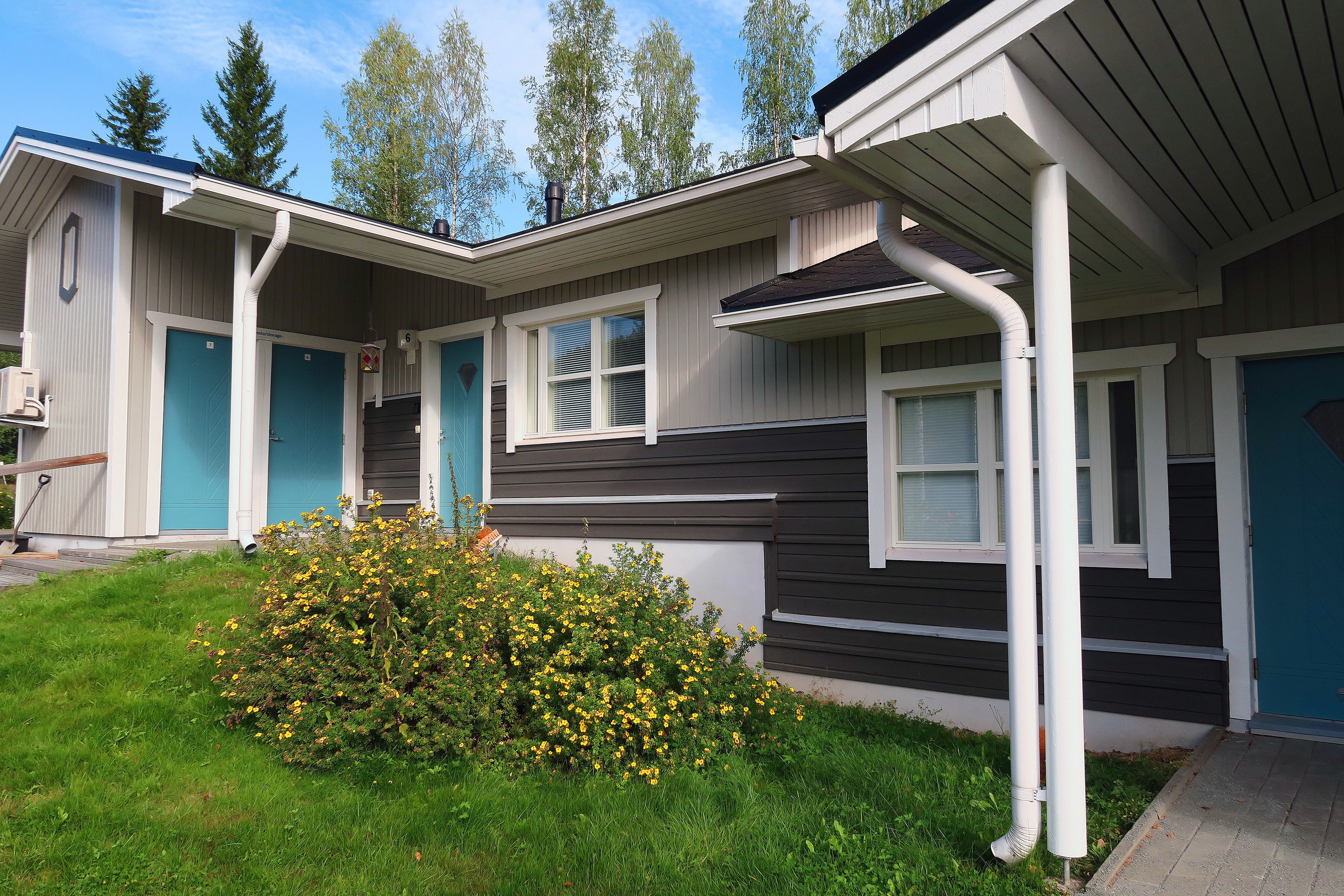 A two-story house with a covered porch, a small garden with yellow flowers, and a blue door.