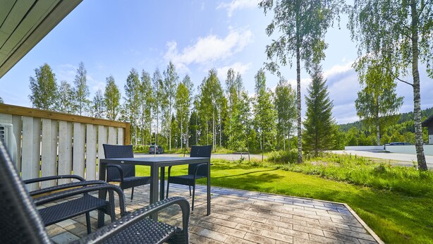 An outdoor patio with a table and chairs, surrounded by a grassy area and trees. - Apartments Huili (Kuopio)