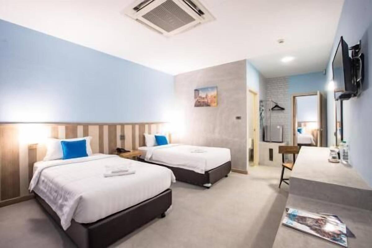 Quarto de hotel com duas camas, uma escrivaninha, uma cadeira, televisão de tela plana e um banheiro pequeno.
