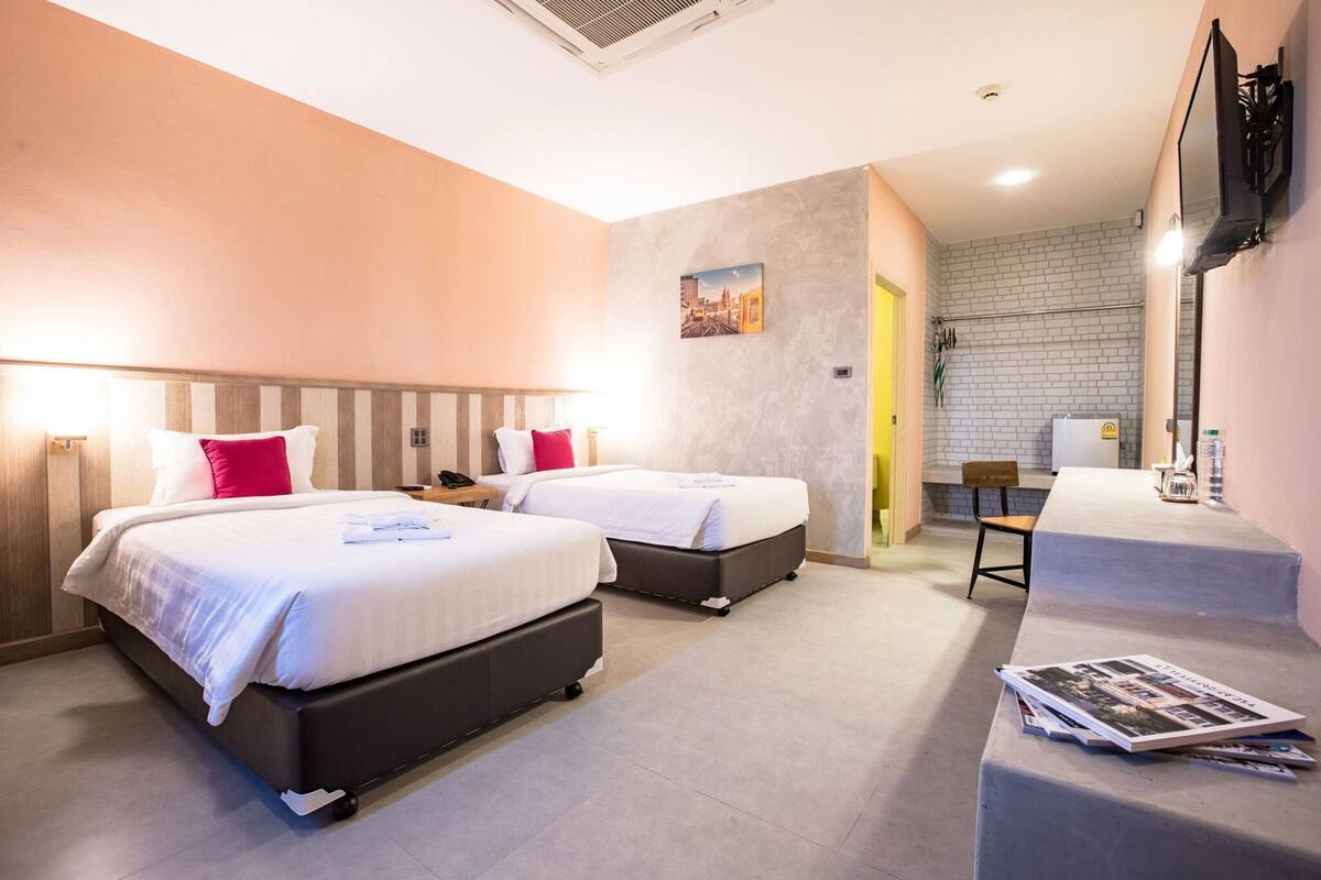 Een hotelkamer met twee bedden, een bureau, een stoel en een aan de muur bevestigde televisie.