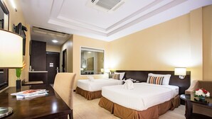 A hotel room with two beds, a desk, a chair, a table with flowers, and a mirror.