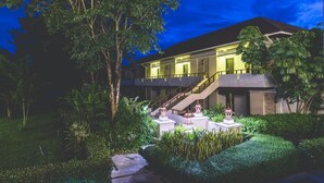 A modern hotel with a well-lit exterior, a staircase leading to the entrance, and a landscaped garden with a water feature and decorative elements.