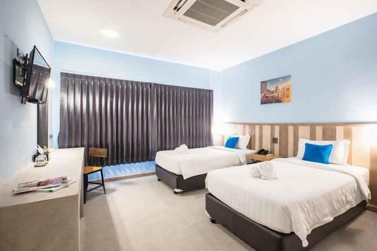 Une chambre d’hôtel avec deux lits, un bureau, une chaise, un téléviseur à écran plat et une fenêtre avec des rideaux.