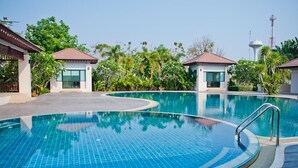 A swimming pool with a tiled deck, surrounded by greenery and small buildings with red roofs.