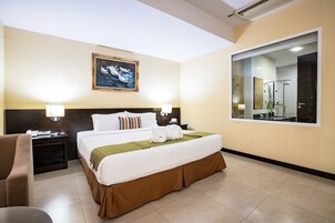 Una habitación de hotel con una cama grande, una mesita de noche con lámpara, una silla y un cuadro en la pared.