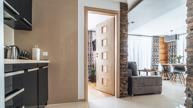 Una cocina moderna con armarios negros, una puerta de madera y un comedor con mesa y sillas.