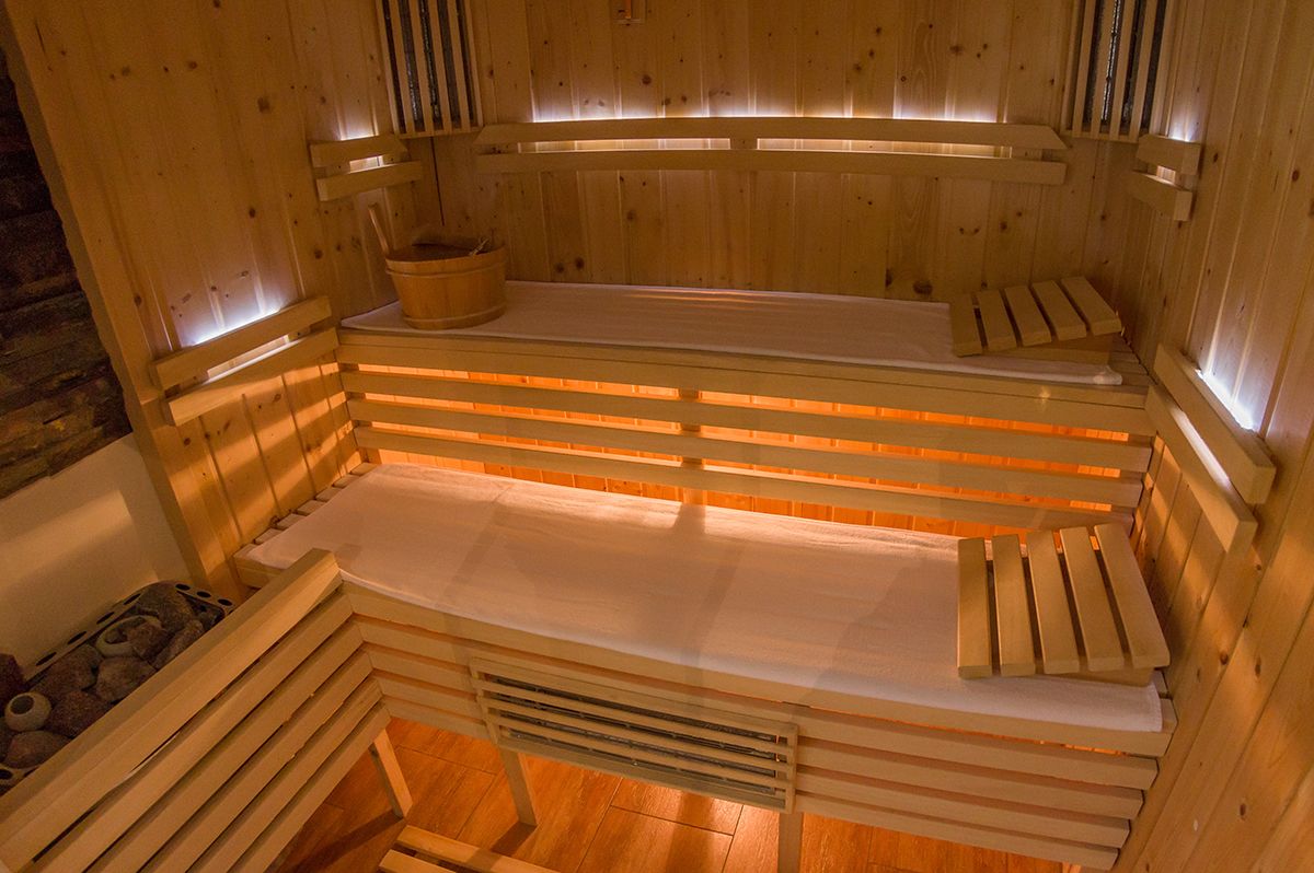 Una sauna de madera con bancos y un asiento, un cubo de madera y una cuenca de piedra.