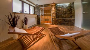 Un spa moderno con tumbonas de madera, pared de piedra y puerta de vidrio que da a una zona de sauna.