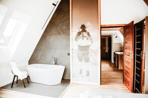 Um banheiro moderno com uma banheira independente, uma cadeira branca e piso de madeira.