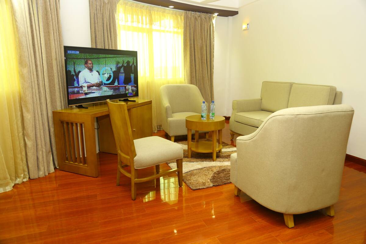 A living room with a television, two armchairs, a sofa, a wooden coffee table, and a small rug.