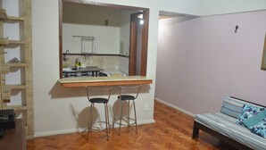A compact living space with a kitchenette, two bar stools, a sofa, and a wooden floor. - Copacabana Etrusco Apartment (Rio de Janeiro)